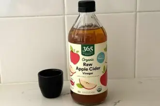 A bottle of Whole Foods 365 raw apple cider vinegar next to a tiny black vase on a marble kitchen counter.