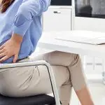 A person sitting down holding their lower back