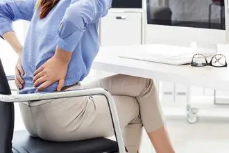 A person sitting down holding their lower back