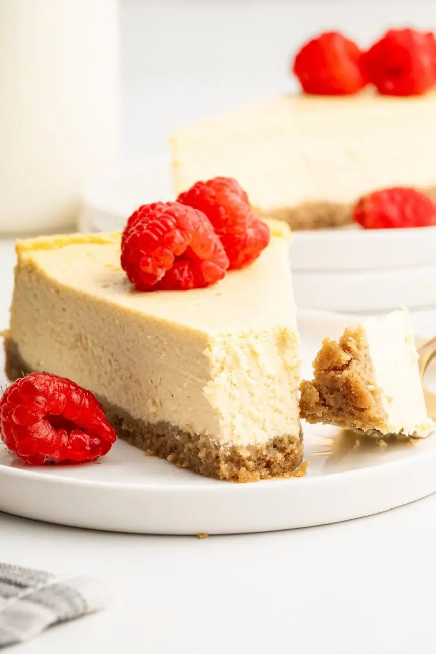 A slice of healthy cheesecake served on a white plate topped with fresh raspberries. A bite has been taken out of the slice.