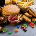 an assortment of unhealthy foods on a table, including a hamburger, fries, candy, chocolate, soda, and a donut