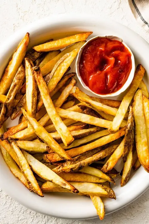 A plate of air fryer french fries with a small container of ketchup on the side.