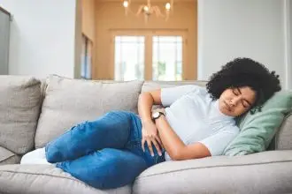 Woman laying on gray couch holding stomach with eyes closed