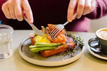 A man&apos;s hands cutting a salmon and avocado flatbread with a knife and fork.