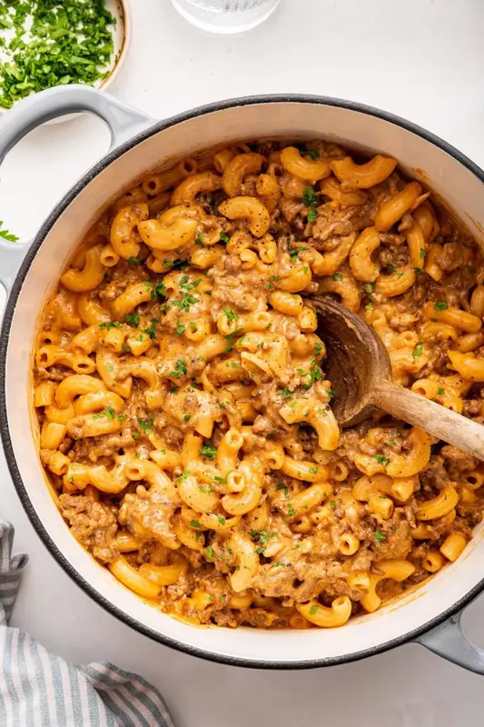 Healthy hamburger helper garnished with fresh herbs, in a large pot with a wooden serving spoon.