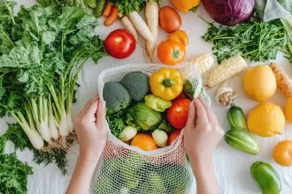 Close-up of hands placing fresh vegetables and fruits into an eco-mesh bag on a white table.