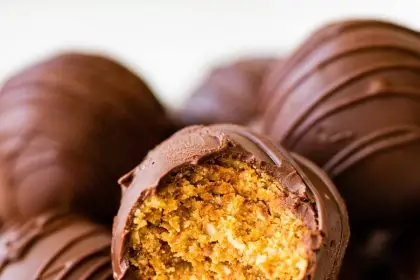 Chocolate covered peanut butter balls in a bowl with one ball having a bite taken from it.