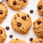 Multiple chocolate chip protein cookies are spread out on a countertop.