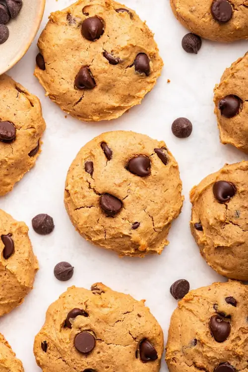 Multiple chocolate chip protein cookies are spread out on a countertop.