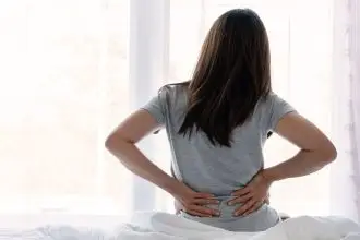 a photo of a woman sat on her bed, holding her lower back