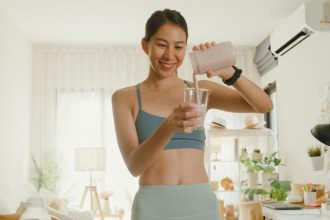 A person with pulled-back dark brown hair and a medium-blue sports bra pouring a smoothie into a glass.