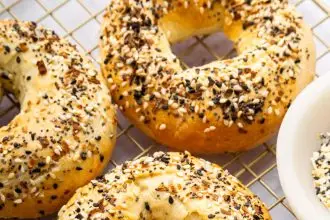 Four everything bagels on a gold cooling rack.