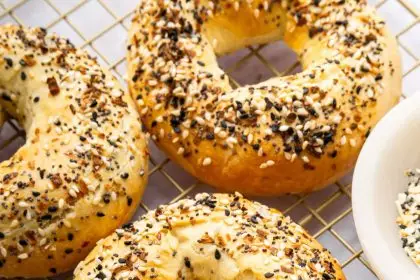 Four everything bagels on a gold cooling rack.