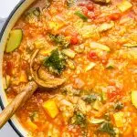 A large pot of vegetable packed quinoa soup with a wooden serving spoon in the soup.