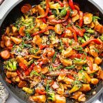 Chicken stir fry with colorful vegetables and tender chicken in a skillet, topped with sesame seeds and green onions.