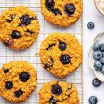 Six sweet potato blueberry oatmeal cookies on a wire cooling rack. Fresh blueberries are scattered next to the rack.