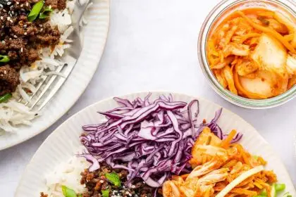 Korean beef served over white rice with fresh carrots, purple cabbage, cucumber and kimchi. The beef is topped with sesame seeds and green onions.