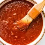 A bowl filled with homemade BBQ sauce with a small brush in the sauce.