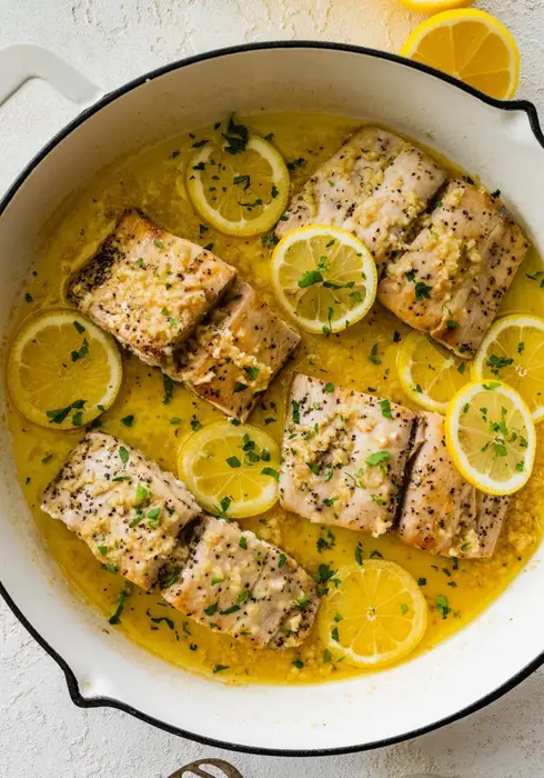 4 Mahi mahi fillets in a skillet with a lemon butter garlic sauce. There are lemon slices in the skillet and everything is topped with fresh parsley.