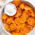 Baked sweet potato chips in a bowl with a small bowl of white dipping sauce.