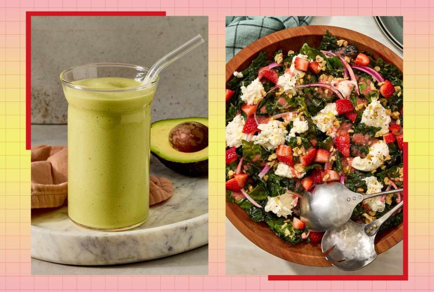 A glass of green smoothie with an avocado on the side a wooden bowl of salad with strawberries and crumbled cheese