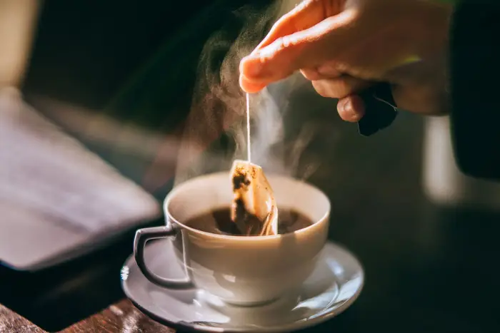 A person dunking a tea bag into a cup of tea a steaming cup on a wooden surface
