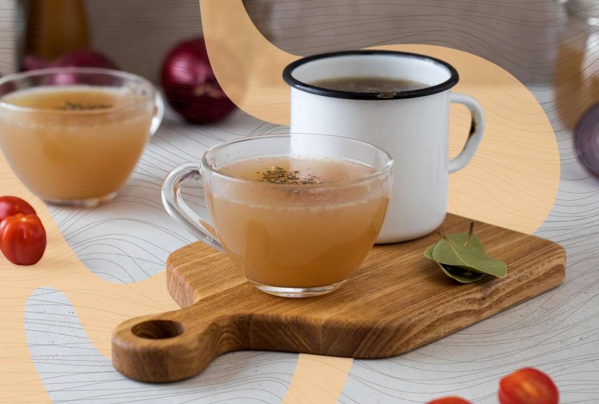 Two cups of bone broth placed on a wooden board garnished with a bay leaf